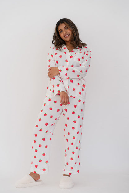 Young woman posing for a photo against a white background, wearing a white pyjama set with a red strawberry pattern