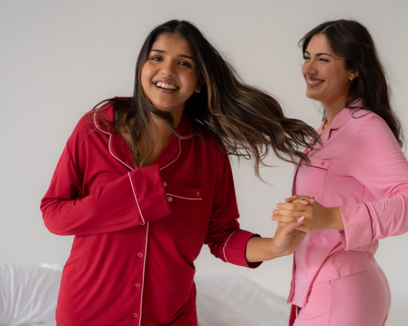 Two women in matching red and pink pajama sets standing on a bed.
